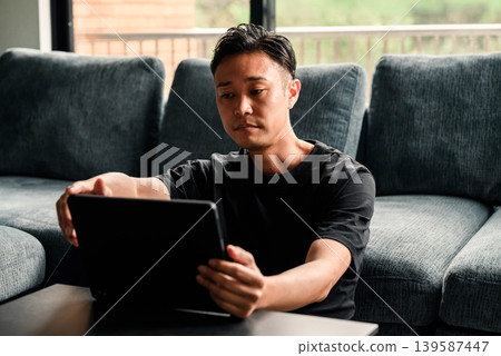 A man looking at a tablet in front of a sofa. 139587447