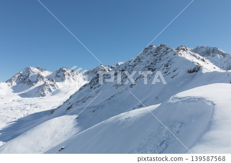 Snowy mountain ridge and ski slopes near Karakol ski resort under blue sky Snowy mountain ridge and ski slopes near Karakol ski resort under blue sky 139587568