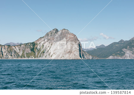 Rocky coastal cliffs and calm sea under clear sky in Kamchatka Peninsula, Russia Rocky coastal cliffs and calm sea under clear sky in Kamchatka Peninsula, Russia 139587814