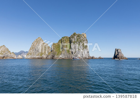 Scenic sea cliffs and rocky islets near Starichkov Island with boat on water Scenic sea cliffs and rocky islets near Starichkov Island with boat on water 139587818