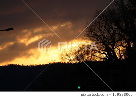 A landscape of silhouetted trees, clouds, and an orange sunset sky. A landscape of silhouetted trees, clouds, and an orange sunset sky. 139588003