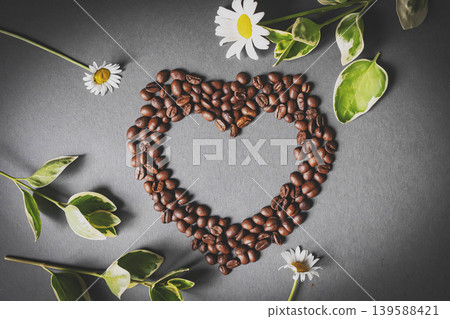 Cafes and restaurants. A mug of invigorating, black coffee and coffee beans in the shape of a heart on a dark gray background. Copy space for text. The concept of hot drinks and love. Cafes and restaurants. A mug of invigorating, black coffee and coffee beans in the shape of a heart on a dark gray background. Copy space for text. The concept of hot drinks and love. 139588421