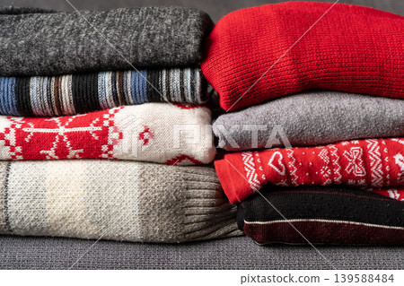 Pile of knitted woolen sweaters autumn colors on wooden table. Clothes with different knitting patterns folded in stack. Warm cozy winter fall knitwear concept. Copy space. Pile of knitted woolen sweaters autumn colors on wooden table. Clothes with different knitting patterns folded in stack. Warm cozy winter fall knitwear concept. Copy space. 139588484