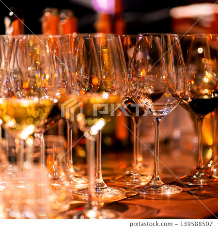 Elegant scene of wine being poured into glasses aligned in a row, showcasing the rich colors and graceful flow of the liquid, set against a dark, warm background, ideal sophisticated dining settings Elegant scene of wine being poured into glasses aligned in a row, showcasing the rich colors and graceful flow of the liquid, set against a dark, warm background, ideal sophisticated dining settings 139588507