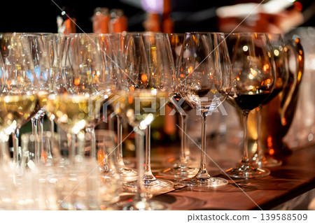 Elegant scene of wine being poured into glasses aligned in a row, showcasing the rich colors and graceful flow of the liquid, set against a dark, warm background, ideal sophisticated dining settings Elegant scene of wine being poured into glasses aligned in a row, showcasing the rich colors and graceful flow of the liquid, set against a dark, warm background, ideal sophisticated dining settings 139588509