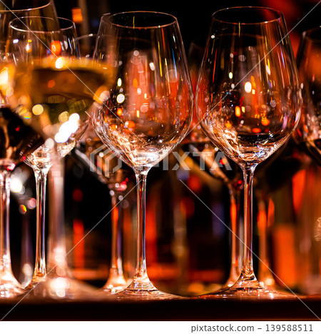 Elegant scene of wine being poured into glasses aligned in a row, showcasing the rich colors and graceful flow of the liquid, set against a dark, warm background, ideal sophisticated dining settings Elegant scene of wine being poured into glasses aligned in a row, showcasing the rich colors and graceful flow of the liquid, set against a dark, warm background, ideal sophisticated dining settings 139588511