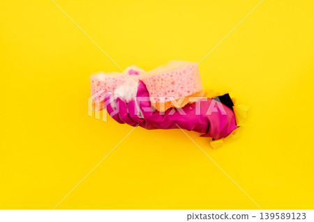 Hand in magenta cleaning glove with soapy sponge through yellow paper 139589123