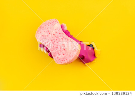 Hand in magenta cleaning glove with soapy sponge through yellow paper 139589124