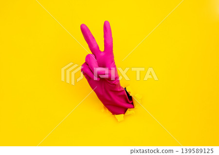 Magenta cleaning glove victory sign through torn yellow paper Magenta cleaning glove victory sign through torn yellow paper 139589125