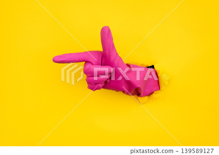 Pink cleaning glove pointing through torn yellow paper background Pink cleaning glove pointing through torn yellow paper background 139589127