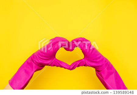 Hands in pink gloves making heart shape on yellow 139589148