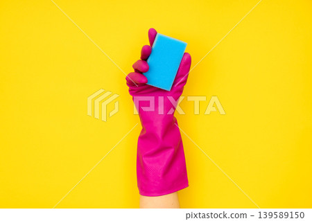 Hand in pink cleaning glove holding blue sponge Hand in pink cleaning glove holding blue sponge 139589150
