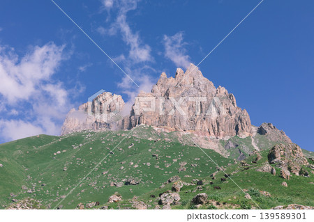 Mount Naudzhidza rocky peak above green alpine meadow under blue sky Mount Naudzhidza rocky peak above green alpine meadow under blue sky 139589301