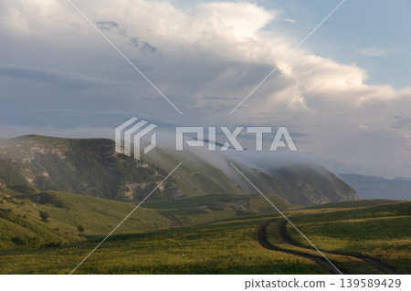 Mountain meadow road with low clouds over Caucasus ridge in Dagestan region 139589429