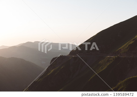 Mountain road on steep ridge at sunset in Dagestan with layered Caucasus peaks 139589472