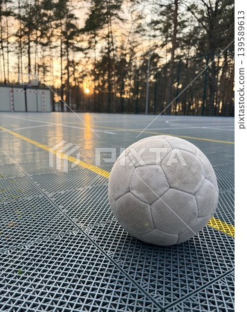 An old soccer ball lies on the artificial surface of a sports stadium in an open wooded area An old soccer ball lies on the artificial surface of a sports stadium in an open wooded area 139589613
