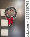 Festive Christmas wreath with red ribbon and ornaments hanging on a modern dark door. Cozy holiday decoration with traditional winter celebration atmosphere 139589765