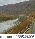 Scenic river landscape with a cruise ship sailing through a winding valley surrounded by forested hills and dramatic cloudy sky. Peaceful travel destination with natural European countryside 139589806