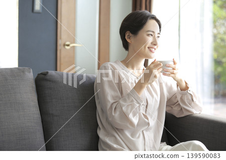 A woman relaxes by the window, sipping coffee during her morning relaxation time. 139590083