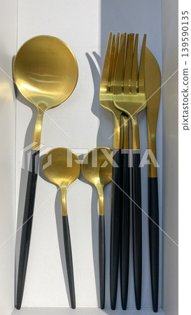 Modern gold cutlery set with matte black handles including spoons, forks, and a knife arranged on a white background Modern gold cutlery set with matte black handles including spoons, forks, and a knife arranged on a white background 139590135
