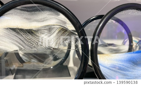 Round kinetic sand art frames with flowing black white and blue sand creating beautiful landscapes Round kinetic sand art frames with flowing black white and blue sand creating beautiful landscapes 139590138