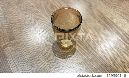 Top view of a single amber glass tumbler on a light wooden table surface with soft shadows Top view of a single amber glass tumbler on a light wooden table surface with soft shadows 139590146