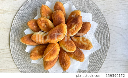 Top view of golden brown fried pirozhki arranged in a circle on white napkins and a round placemat 139590152