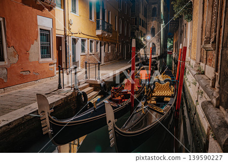 Elegant Venetian gondolas on quiet canal at night with glowing reflections Elegant Venetian gondolas on quiet canal at night with glowing reflections 139590227