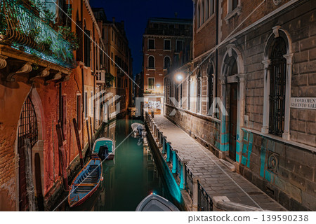 Quiet Venice canal at night with bridge, boats and glowing street lights 139590238