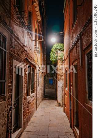 Narrow Venetian alley at night with glowing lamps and silent atmosphere 139590240