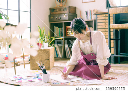 A young Japanese woman painting on the living room floor. A young Japanese woman painting on the living room floor. 139590355