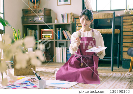 一位年輕的日本女子正在客廳地板上作畫。 一位年輕的日本女子正在客廳地板上作畫。 139590363