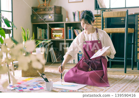 A young Japanese woman painting on the living room floor. A young Japanese woman painting on the living room floor. 139590416
