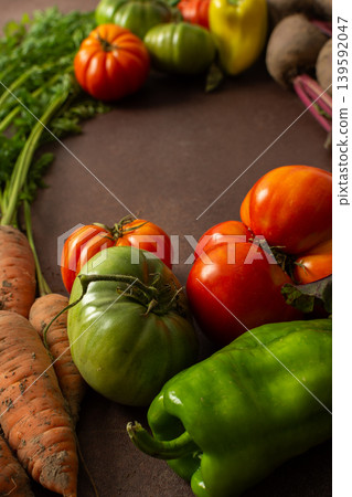 Fresh carrots sit next to red and green tomatoes along with bell peppers on a brown surface. The scene shows a variety of vegetables gathered for cooking or selling Fresh carrots sit next to red and green tomatoes along with bell peppers on a brown surface. The scene shows a variety of vegetables gathered for cooking or selling 139592047