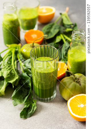 Fresh juice is made using spinach, chard, and broccoli along with oranges and tangerines. A glass of green juice sits by fresh ingredients on a clean kitchen counter 139592057