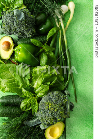 A vibrant collection of fresh green vegetables and herbs fills the scene, showcasing broccoli, cucumbers, lettuce, avocado, and various herbs like basil and dill, healthy eating 139592088