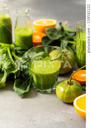 Fresh juice is made using spinach, chard, and broccoli along with oranges and tangerines. A glass of green juice sits by fresh ingredients on a clean kitchen counter 139592222