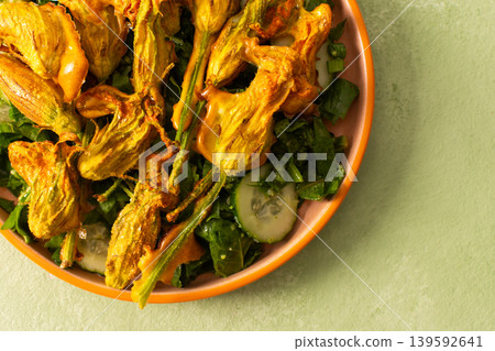 Roasted zucchini flowers are placed on a bed of fresh greens, cucumbers, and broccoli during a summer meal. This dish highlights the flavors of summer ingredients Roasted zucchini flowers are placed on a bed of fresh greens, cucumbers, and broccoli during a summer meal. This dish highlights the flavors of summer ingredients 139592641