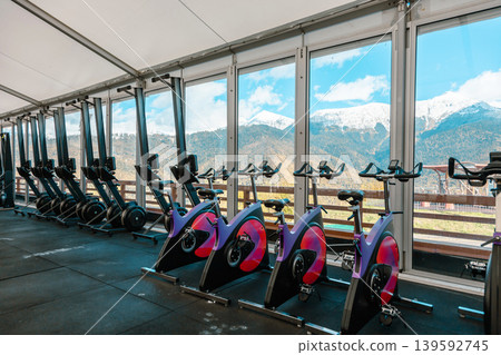 Exercise bikes and rowers in fitness center with scenic mountain landscape 139592745