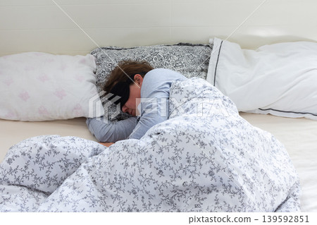 A 50-year-old woman is comfortably sleeping in her bed with a sleep mask on. She is wrapped in a soft blanket, resting peacefully in a serene bedroom setting 139592851