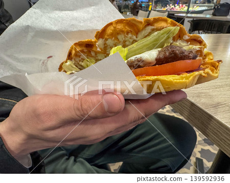 Waffle burger with beef patty, cheese, lettuce and tomato in hand, street food in cafe close-up Waffle burger with beef patty, cheese, lettuce and tomato in hand, street food in cafe close-up 139592936