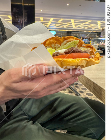 A Viennese waffle burger with beef patty, cheese, lettuce and tomato in hand, a fast food sandwich in a shopping mall food court 139592937