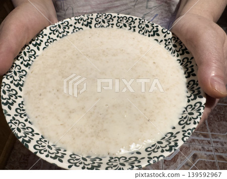 Creamy oatmeal porridge in patterned bowl held in hands, homemade warm breakfast close-up in kitchen Creamy oatmeal porridge in patterned bowl held in hands, homemade warm breakfast close-up in kitchen 139592967