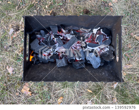 Smoldering coals in a portable metal grill, close-up of an outdoor barbecue with hot coals for shashlik Smoldering coals in a portable metal grill, close-up of an outdoor barbecue with hot coals for shashlik 139592976