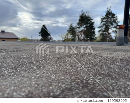 Bottom view of rough asphalt road surface, urban road surface texture with blurred trees and cloudy sky in the background Bottom view of rough asphalt road surface, urban road surface texture with blurred trees and cloudy sky in the background 139592995