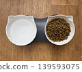 White double cat food bowl with dry food on wooden floor, pet feeding station 139593075