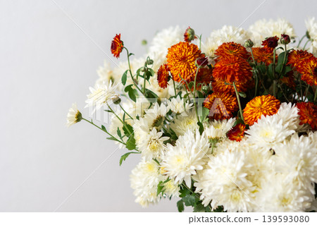 A white pitcher filled with orange and white flowers sits on a light surface. This setup can be used for home decoration or floral arrangement inspiration A white pitcher filled with orange and white flowers sits on a light surface. This setup can be used for home decoration or floral arrangement inspiration 139593080