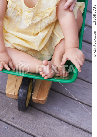 Baby, child and riding toy wagon in outdoors, plastic and fun activity for childhood. Kid, toddler and wheelbarrow for playing games on porch or deck, closeup and relaxing in construction equipment Baby, child and riding toy wagon in outdoors, plastic and fun activity for childhood. Kid, toddler and wheelbarrow for playing games on porch or deck, closeup and relaxing in construction equipment 139593738