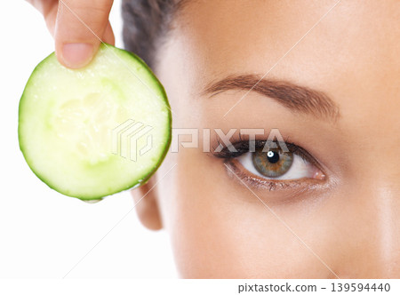 Woman, face and cucumber by eyes in beauty, facial or spa treatment on a white studio background. Closeup of female person and natural organic vegetable for anti aging benefits in health and wellness Woman, face and cucumber by eyes in beauty, facial or spa treatment on a white studio background. Closeup of female person and natural organic vegetable for anti aging benefits in health and wellness 139594440