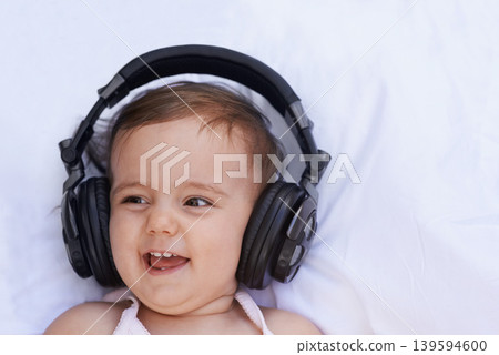 Baby, headphones and listening to song for fun, above and face on bed at home. Child, happiness and hearing audio for child development or learning, toddler and calming playlist for peace and calm Baby, headphones and listening to song for fun, above and face on bed at home. Child, happiness and hearing audio for child development or learning, toddler and calming playlist for peace and calm 139594600